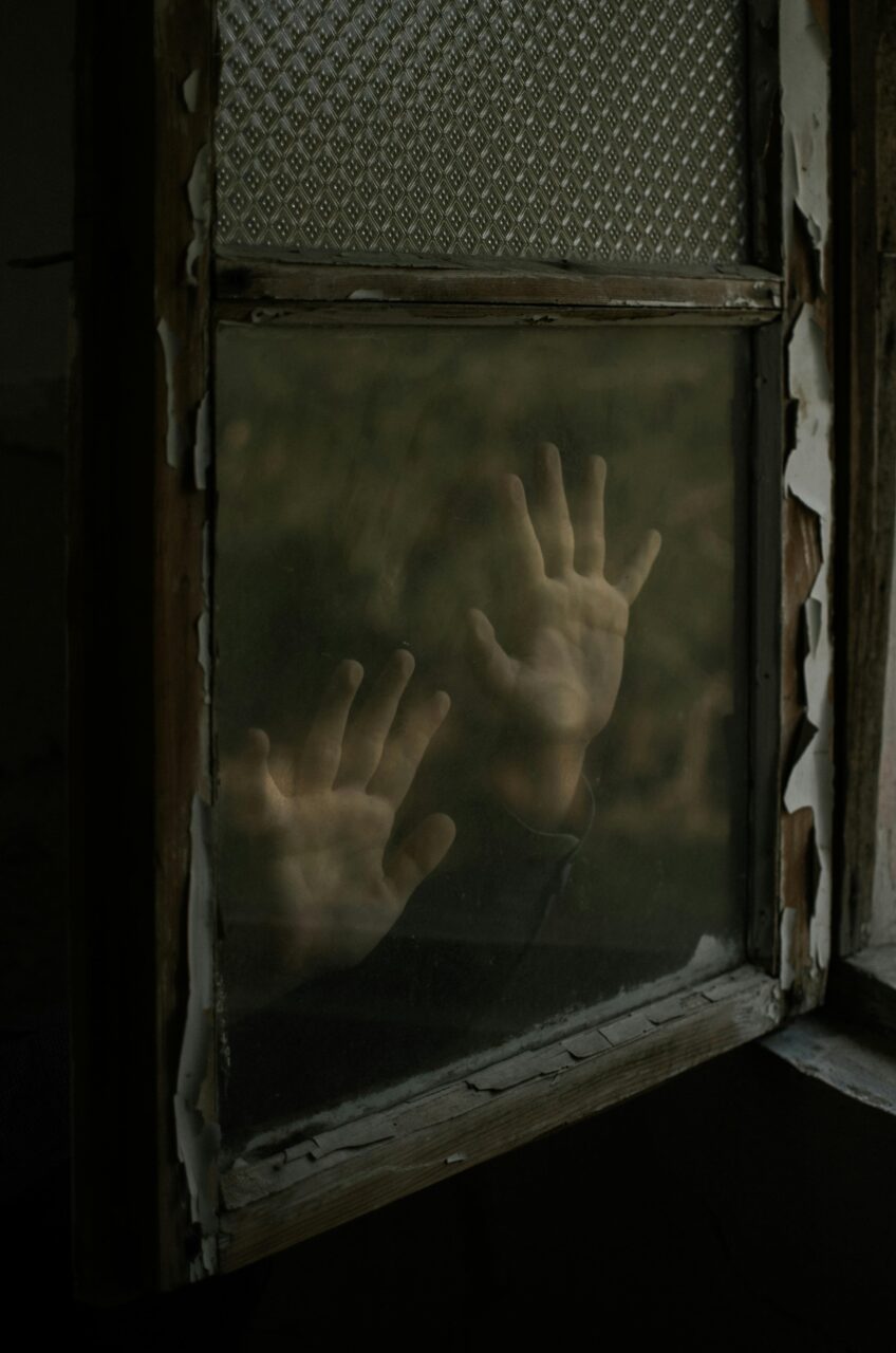 Person holds hands against glass window pane.