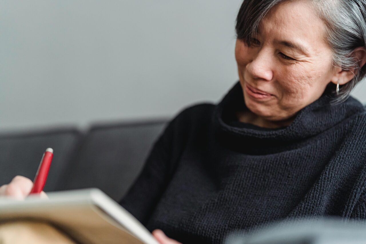 Woman in Black Turtleneck Sweater Smiling and writing on a notepad
